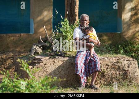 NOVEMBER 15 2022, KACHANDA, CHHATTISGARH, INDIA: Grandfather holding grandson in indian village and sitting under the tree in morning sunlight. Grandf Stock Photo