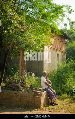 NOVEMBER 15 2022, KACHANDA, CHHATTISGARH, INDIA: Grandfather holding grandson in indian village and sitting under the tree in morning sunlight. Grandf Stock Photo