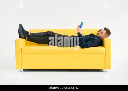 Relaxed man lying on yellow sofa using smartphone Stock Photo