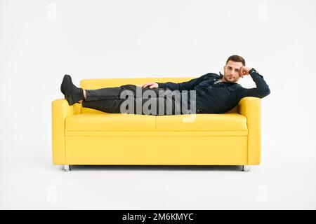 Young man relaxing alone on yellow sofa at home Stock Photo
