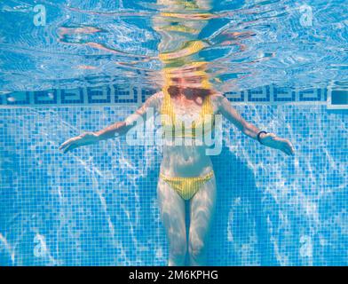 Woman in yellow swimming suit in clear blue water in pool Stock Photo