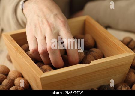hand taking nuts out of a wooden box standing on the table Stock Photo