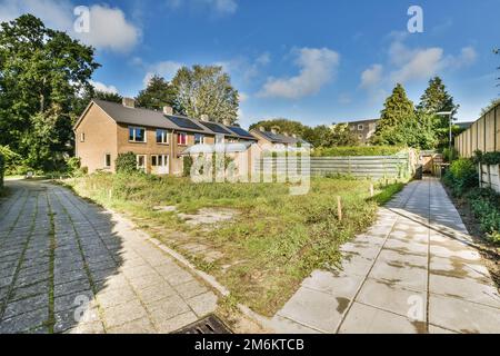 an empty yard in the middle of a residential area with trees and bushes on either side, blue sky above Stock Photo