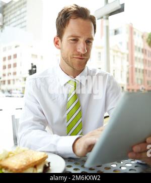 Working through his break. A young businessman working on his digital tablet while sitting at an outdoor cafe. Stock Photo