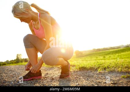 Putting on her running shoes. A young woman in sportswear tying her shoelaces. Stock Photo