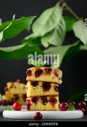 Baked pieces of sponge cake with red ripe cherries on a white wooden board Stock Photo