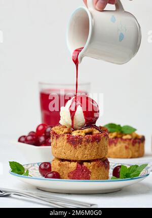 Cherry crumble pie decorated with a scoop of ice cream and poured with cherry sauce on a plate Stock Photo