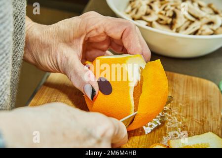 Chef cuts oranges to prepare salad with zucchini, oranges and salami. French gourmet cuisine, on a wooden background. Stock Photo