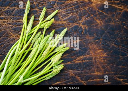 Raw green wild asparagus offered as top view on a rustic burnt wooden board with copy space right Stock Photo