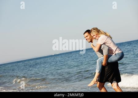 Dont let me get wet. a young man giving his girlfriend a piggyback by the sea. Stock Photo