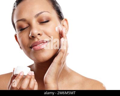 Feel the smoothness. a beautiful young woman applying face cream while standing in a studio. Stock Photo