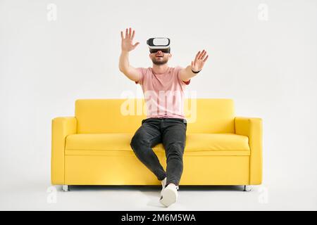Young man in virtual reality headset playing video games and trying to touch something with hands Stock Photo
