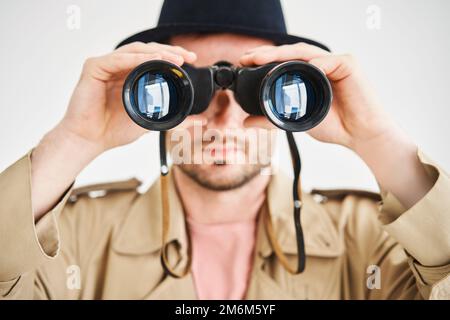 Young man wearing in coat and hat looking through binoculars over isolated white background Stock Photo