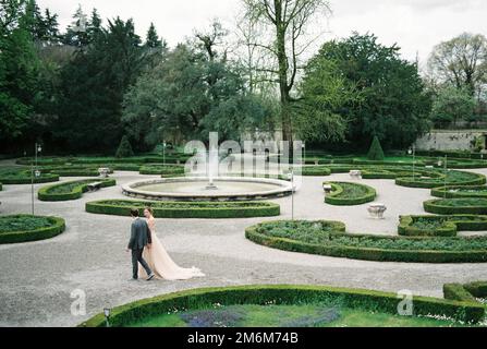Bride and groom holding hands walk in the park near the fountain Stock Photo