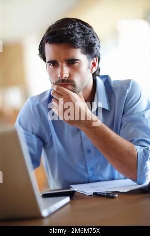 Contemplating his corporate situation. A thoughtful young businessman working on his laptop at his desk. Stock Photo