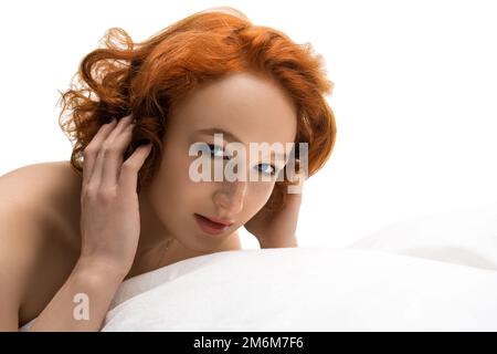 Smile redhead young woman lying in bed and hiding under the pillow Stock Photo
