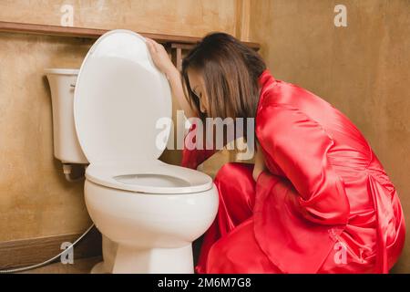 A woman in a red nightgown vomiting in the bathroom Stock Photo