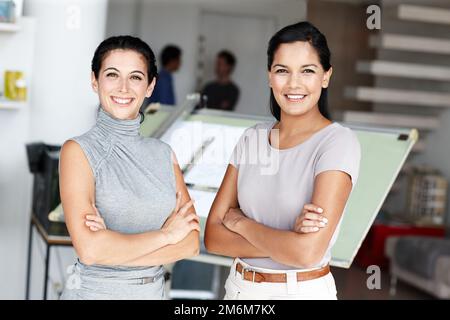 Successful female architects. Two confident architects crossing their arms and standing in front of their blueprints. Stock Photo