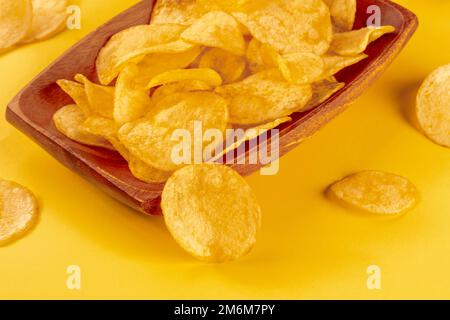 Potato chips or crisps in a bowl and scattered on a yellow background Stock Photo