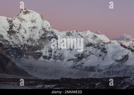 Subset lights over the mountain Cholatse summit in Himalayas, Nepal. Highlands scenery of the mountain range in pinkish sunset light. Beautiful backgr Stock Photo