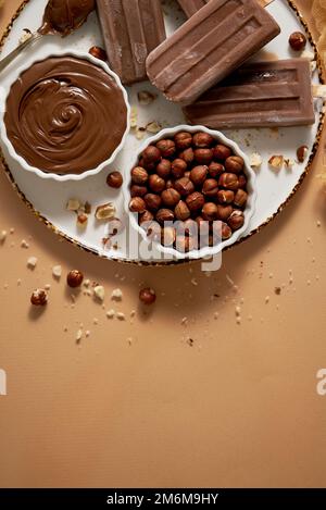 Chocolate popsicles with hazelnuts served with melted chocolate on a white plate Stock Photo
