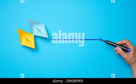 Two paper boats and a woman's hand with a marker on a blue background. The concept of indicating the way forward. Stock Photo