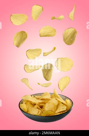 Corrugated fried potato chips falling into a gray plate on a pink background Stock Photo
