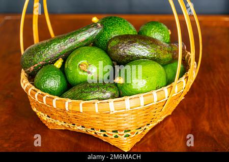 Pile of different varieties of fresh green avocado in wicker bamboo basket. Stock Photo