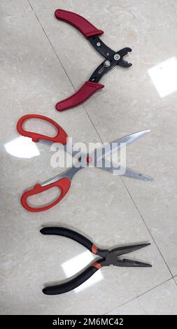 various cutting tools like scissor, cutting plier and wire stripper used in the electronics lab placed on a white floor Stock Photo