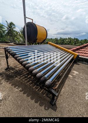 an eco friendly solar water heater and tank installed on the roof of a building for generating hot water renewably Stock Photo