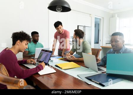 Multiracial male colleagues discussing and co-working over laptops on desk in office, copy space Stock Photo