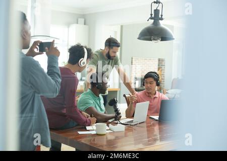 Multiracial male colleagues interviewing and recording podcast and young man filming with smartphone Stock Photo