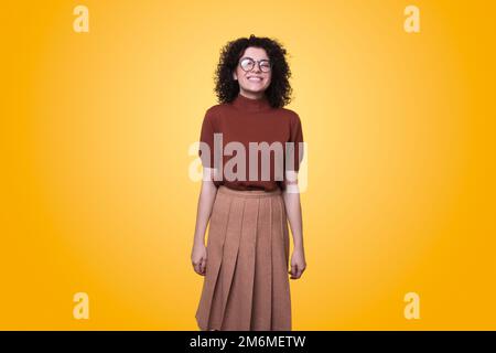 Young friendly woman wearing looking at camera and smiling standing against yellow background. Positive person. People lifestyle. Stock Photo
