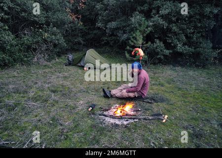man sitting and drinking nearby campfire in Sicily, Etna Park, Italy (backpack) Stock Photo