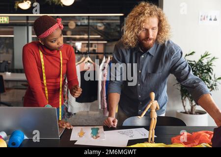 Multiracial male and female fashion designers discussing over sketch at desk in office Stock Photo