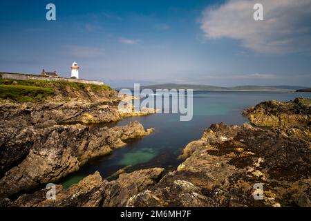 Rocky shoreline with turquoise pools and the historic Broadhaven Lighthouse on a clifftop promontory at the entrance of Broadhav Stock Photo