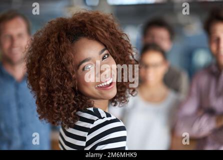 Im making the best of my work life. Beautiful businesswoman smiling with friendly coworkers in the background. Stock Photo