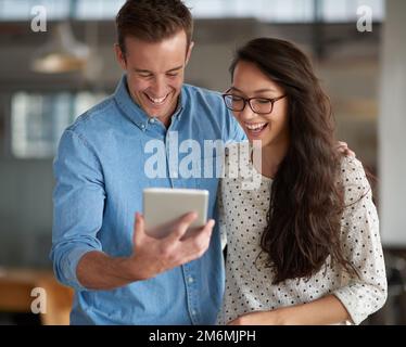 I cant believe it. Friendly colleagues laughing at something funny on a digital tablet at the office. Stock Photo