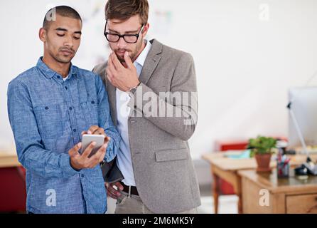 Interesting work. two coworkers standing in an office looking at a digital tablet. Stock Photo