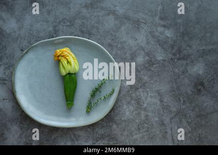 Zucchini flower on gray plate with aromatic herbs on stone background. Horizontal photo. Stock Photo