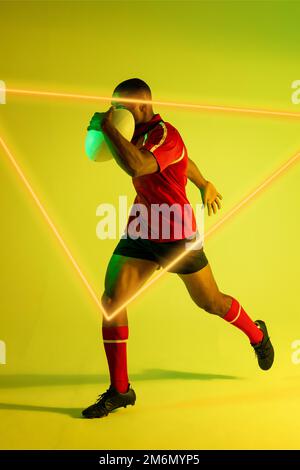 African american male player with rugby ball running by illuminated triangle over green background Stock Photo