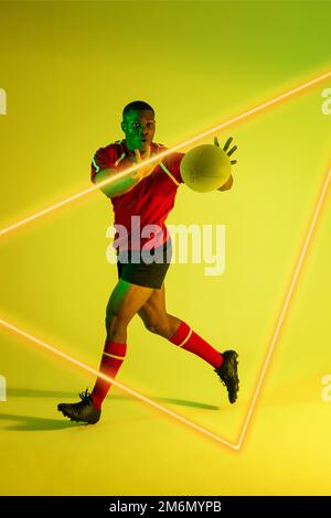 African american male player throwing rugby ball by illuminated triangle over green background Stock Photo