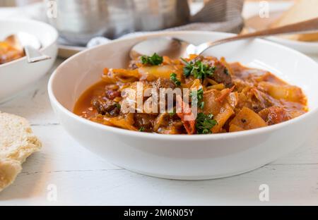 Beef stew with cabbage and vegetables in a bowl on kitchen table. Closeup and front view Stock Photo