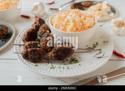 Cevapcici, serbian meatballs served on skewers with delicious homemade american coleslaw on white background Stock Photo