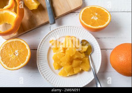 Chopped or diced oranges on a white plate for healthy snack or dessert on white background with cutting board, peel and knife Stock Photo