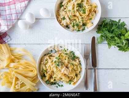 Tagliatelle noodles with scrambled eggs and parsley on plates served on white background with ingredients Stock Photo