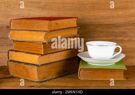 Closeup view stack of colorful old books with white ceramic coffee cup on wooden table. Stock Photo