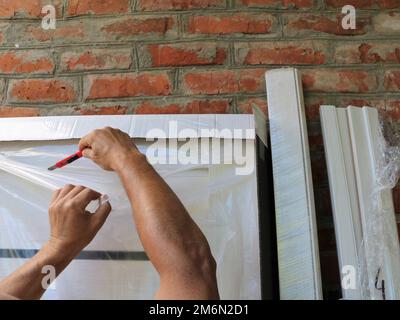 removing the packaging film from the delivered door leaf made of light material with a clerical knife, unpacking the polyethylene of a wooden door Stock Photo