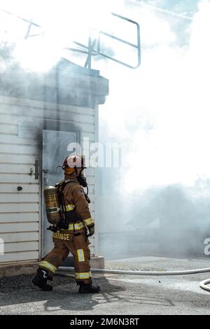 A 316th Civil Engineer Squadron firefighter checks the perimeter of a simulated building fire during an interagency fire-fight training at Joint Base Andrews, Md., May 2, 2022. The team trained in a live-burn exercise to practice firefighting techniques and procedures in a realistic environment, ensuring they are prepared to mitigate damage and save lives. Stock Photo