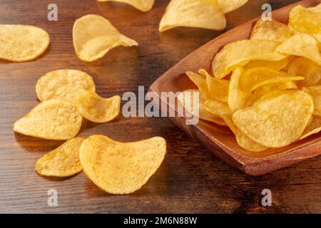 Potato chips or crisps in a bowl and scattered on a wooden background Stock Photo